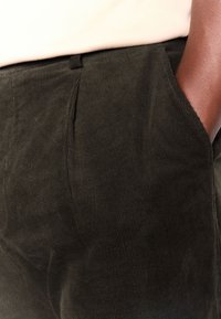 Pantalon en velours côtelé vert foncé avec une texture douce, doté de poches latérales et d'une coupe droite. Motif côtelé subtil sur toute la surface.