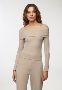 Beżowa bluzka typu off-the-shoulder z prążkowanego materiału, z długimi rękawami, z teksturowanym wzorem i dopasowanym krojem, który podkreśla sylwetkę.
