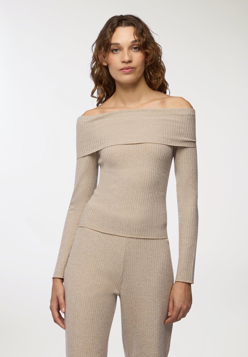 Beżowa bluzka typu off-the-shoulder z prążkowanego materiału, z długimi rękawami, z teksturowanym wzorem i dopasowanym krojem, który podkreśla sylwetkę.