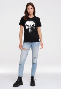 Black cotton t-shirt featuring a white skull graphic, paired with light blue ripped jeans and black lace-up boots.