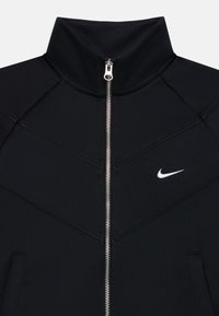 Veste Nike noire avec un col haut, dotée d'une fermeture éclair argentée et d'un petit logo blanc sur la poitrine gauche. Design texturé et sportif.
