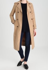 Beige trenchcoat med dubbelknäppning, stora slag och knappdetaljer. Matchad med mörka jeans och svarta slip-on skor.