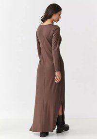Brązowa, długa sukienka maxi z prostą sylwetką, bocznym rozcięciem i gładką fakturą materiału. Posiada okrągły dekolt i minimalne zdobienia.