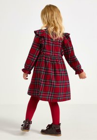 Rødternet kjole med flæseærmer, tætsiddende talje og flagrende nederdel. Kombination med røde leggings og glansfulde sorte ankelstøvler.