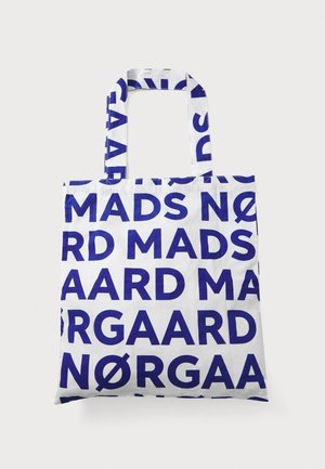 Weiße Tote-Tasche mit blauen fetten Buchstaben, die das Muster "Mads Nørgaard" wiederholen, mit zwei Griffen und quadratischer Form.