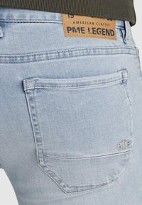 Svijetloplave traperice s stražnjim džepom, s bež kožnom etiketom na kojoj piše "PME LEGEND" i bijelim šavovima.
