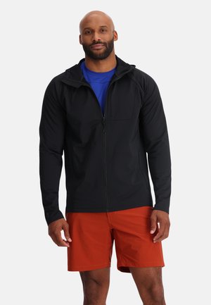 Black zip-up jacket with a hood, textured fabric, and a zippered pocket on the chest, worn over a blue shirt and orange shorts.