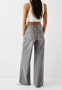 Wide-leg gray jeans made of denim, featuring a high waist, low back pockets, and a subtle faded texture. Hem reaches above the ankle.