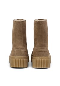 Bottes cheville en daim marron avec une semelle côtelée couleur caramel et une doublure douce. Elles comportent une étiquette logo à l'arrière. Design simple et élégant.