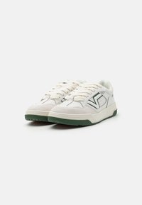 Hvide sneakers med grønne gummisåler og svampeindsatser. Har en snørebåndsdesign og kontrasterende sorte syninger.