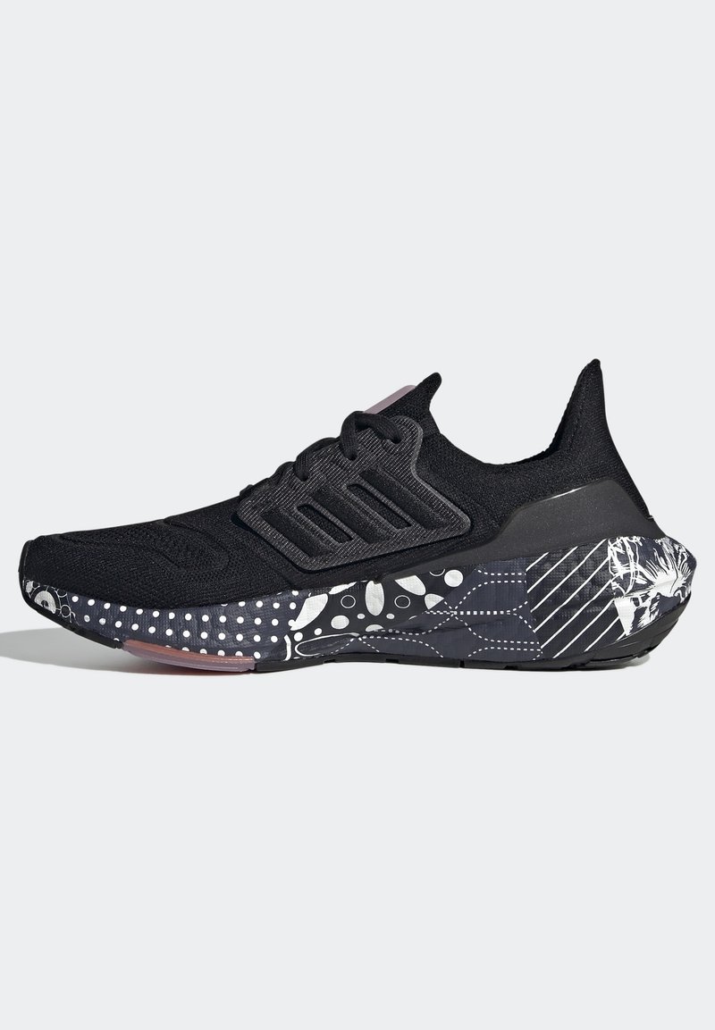 Scarpa sportiva nera con superficie testurizzata, design a tre strisce e suola in gomma a motivo con punti bianchi e accenti grafici.