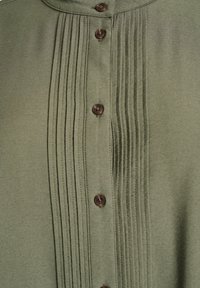 Olivgrön skjorta med knappar fram, plisserad front, bruna knappar och slät textur. Har krage och rak fåll.