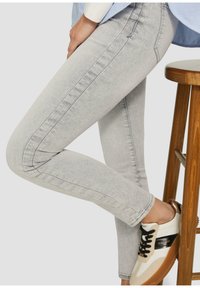 Helle graue Skinny-Jeans mit glatter Textur, seitlichen Nähten und einem subtilen Waschungseffekt. Kombiniert mit einem weißen und braunen Sneaker.