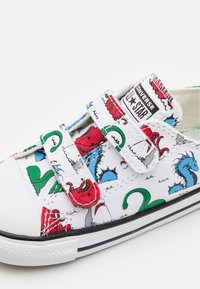 Vit kanvas sneaker med färgglada monster- och varelsemönster, dubbla kardborreband, svart gummisul och tåhätta.