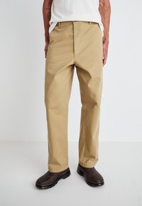 Khaki chinos with a straight-leg cut, made of cotton. Details include belt loops and front pockets, paired with dark brown shoes.