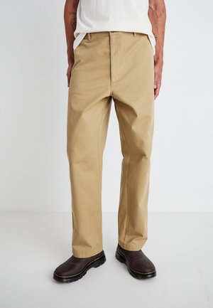 Khaki chinos with a straight-leg cut, made of cotton. Details include belt loops and front pockets, paired with dark brown shoes.