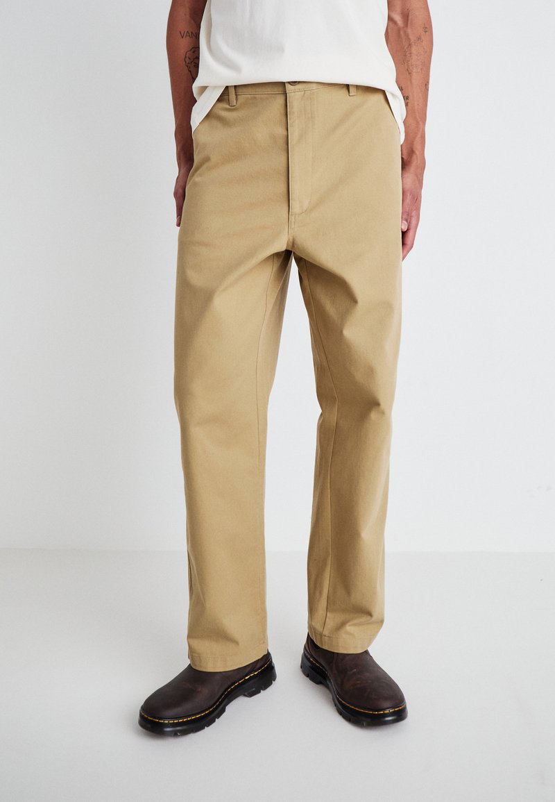 Khaki chinos with a straight-leg cut, made of cotton. Details include belt loops and front pockets, paired with dark brown shoes.