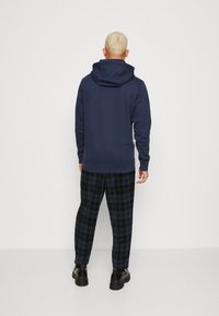 Sudadera azul marino con capucha ajustable, combinada con pantalones de cuadros en negro y azul. El conjunto cuenta con puños acanalados y un corte relajado.
