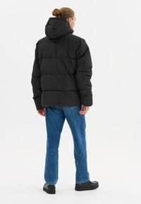 Doudoune noire avec capuche, présentant un design matelassé et une coupe ample. Portée avec un jean bleu et des chaussures à plateforme noires.