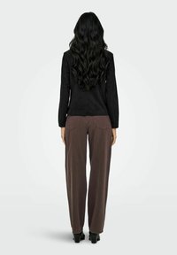 Veste noire à manches longues associée à un pantalon brun ample. La veste présente une coupe ajustée, tandis que le pantalon est large et possède des poches arrière.