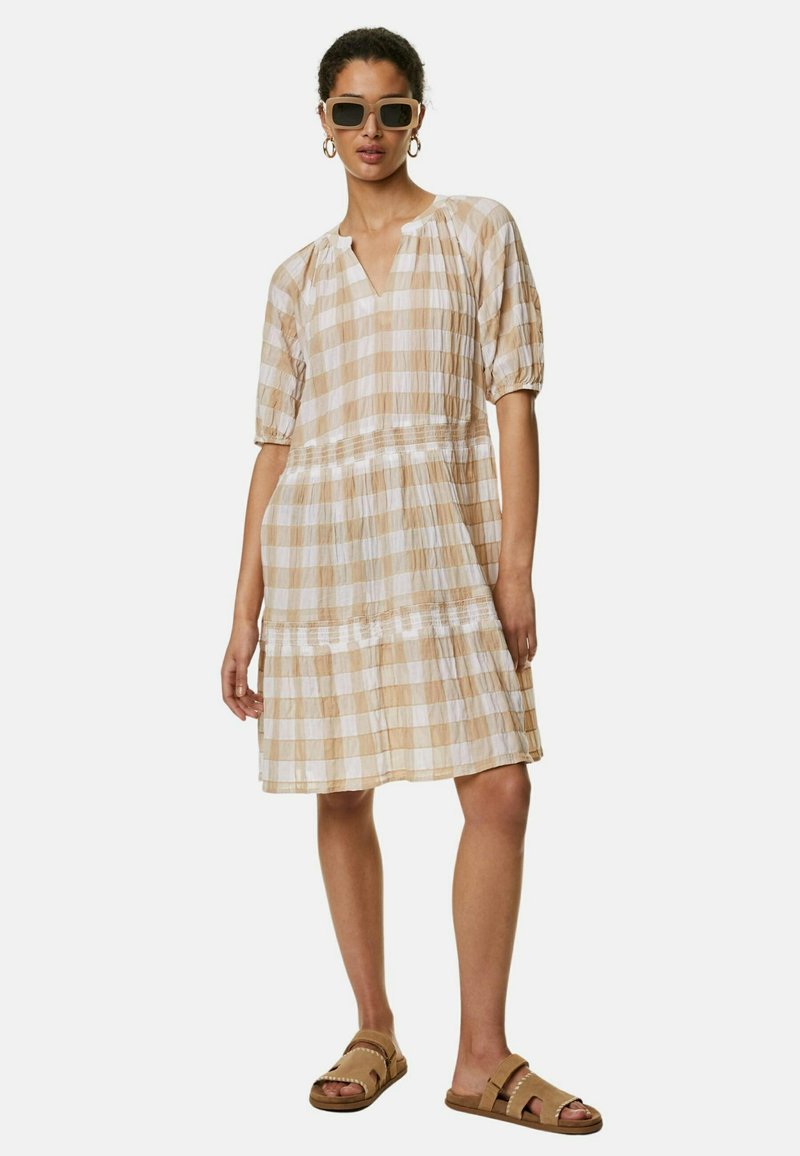 Ljust brunt och krämfärgat rutigt klänning med puffärmar, v-ringning och draperad midja, tillsammans med bruna sandaler och solglasögon.