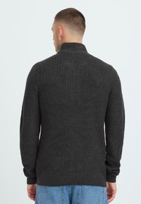 Kullgrå genser med høy krage, teksturert strikkemønster og lange ermer, sammen med lyse denimjeans, vist fra ryggen.