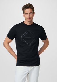 Camiseta de algodón negra con un logotipo geométrico brillante en el centro. Mangas cortas, cuello redondo, textura suave y corte holgado.