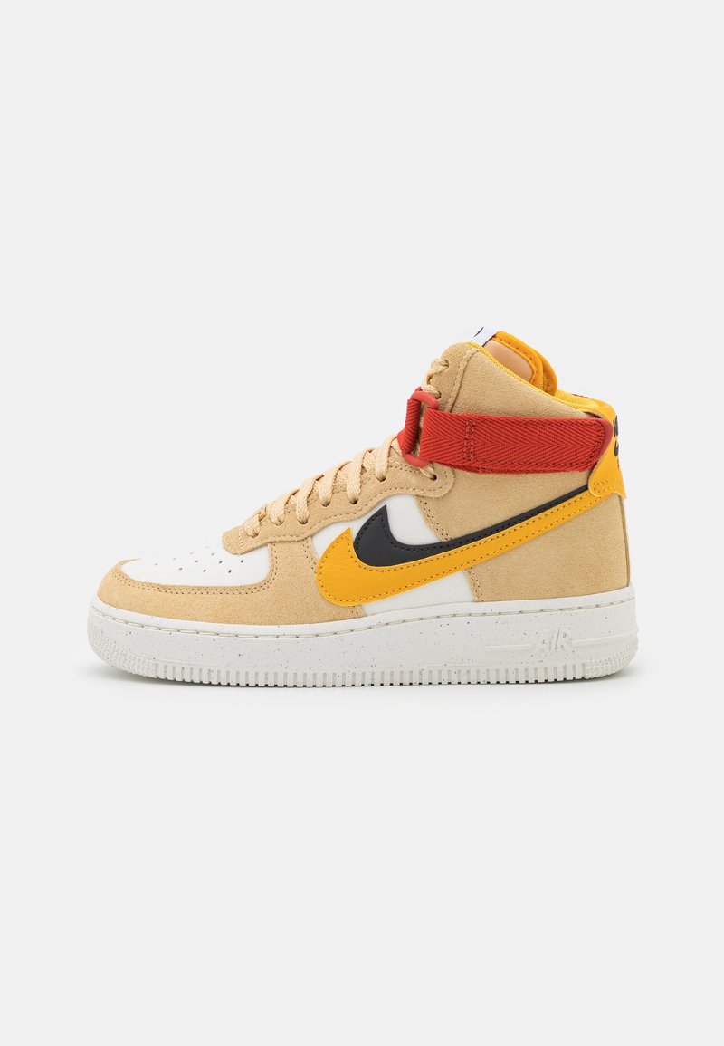 Kopačky Nike Air Force 1 mají svršek z hnědé semišové kůže, bílou špičku a oranžové, černé a červené akcenty. Vysoký design s texturovanou podrážkou.