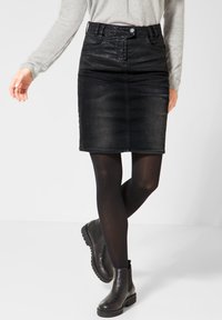 Musta farkku kynähame, jossa on etunappikiinnitys, sivutaskut, puolipitkä malli, yhdistettynä opakkisiin mustiin sukkahousuihin ja mustiin nilkkabootseihin.