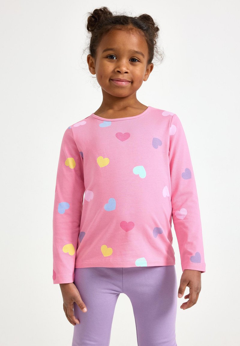 Maglietta a maniche lunghe rosa con motivi a cuore multicolore, abbinata a leggings lavanda. Tessuto morbido con scollo rotondo.