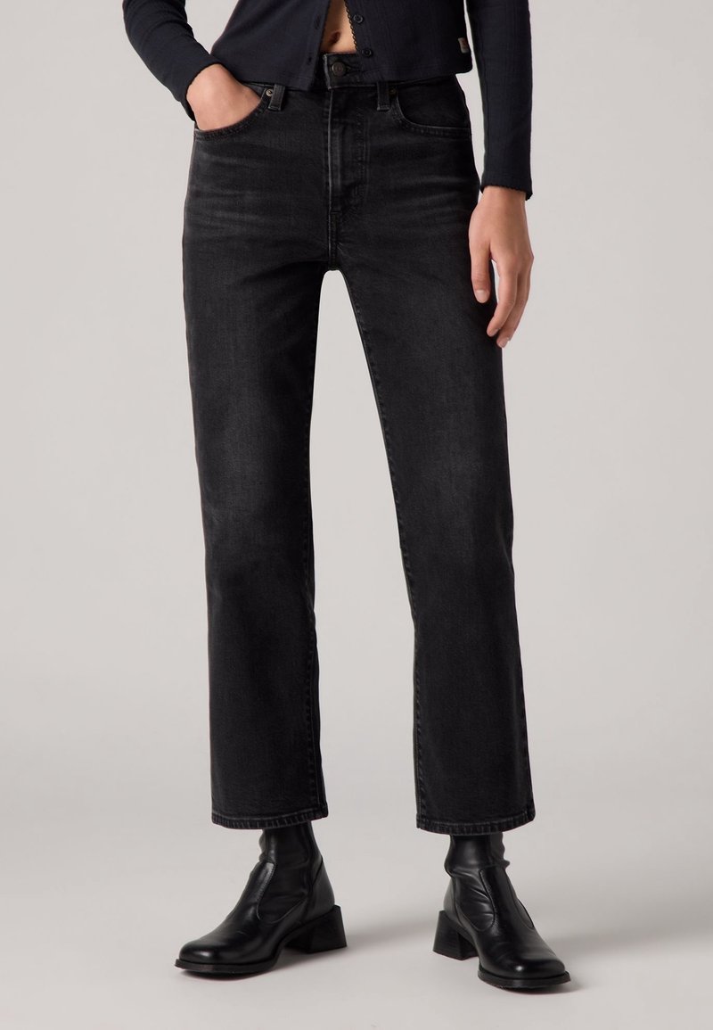 Jean en denim noir avec une coupe droite, un design à cinq poches et des détails de couture visibles. Portés avec des bottines noires.