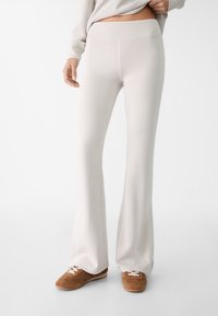 Rozšířené světle béžové kalhoty vyrobené z měkké tkaniny, s hladkým pasem a elegantním, štíhlým designem. Doplněné hnědými teniskami.