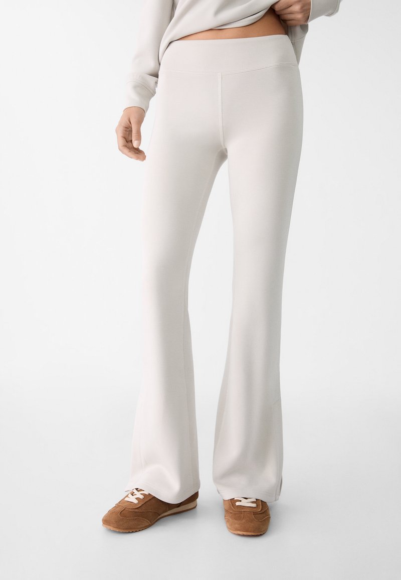 Rozšířené světle béžové kalhoty vyrobené z měkké tkaniny, s hladkým pasem a elegantním, štíhlým designem. Doplněné hnědými teniskami.