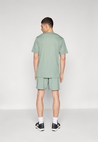 Hellgrünes Sportshirt und Shorts mit weißen Seitenstreifen, getragen mit schwarzen Schuhen und weißen Socken. Einfaches Design, lässige Passform.