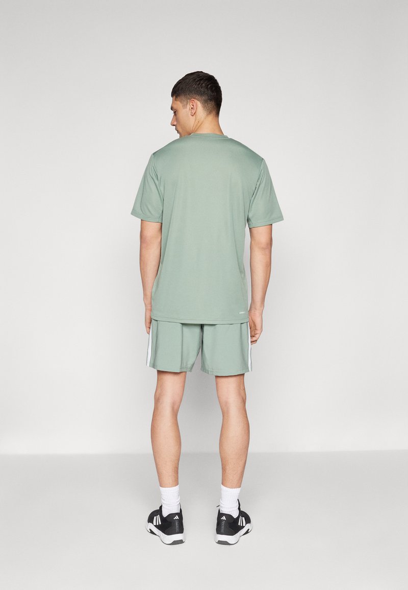 Camiseta y pantalones cortos deportivos verde claro con franjas laterales blancas, combinados con zapatos negros y calcetines blancos. Diseño sencillo, ajuste casual.