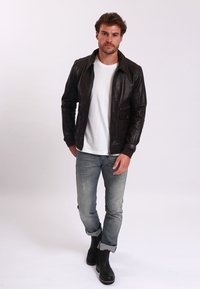 Bruine leren jas met ritszakken, gedragen over een witte T-shirt. Licht versleten jeans en zwarte enkelboots. Eenvoudig, op maat gemaakt ontwerp.