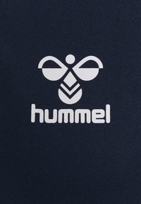 Mørkeblåt stof med et hvidt logo, der har stiliserede vinger og en nedadgående pil, ledsaget af mærkenavnet "hummel" i fed skrifttype.
