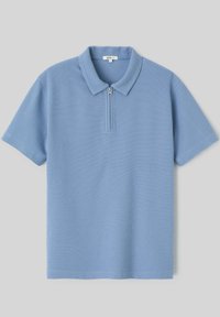 Polo bleu clair à manches courtes avec col et fermeture éclair à l’avant sur un fond neutre.