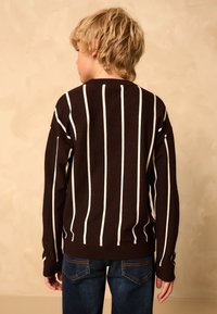 Brun randig tröja med vita vertikala linjer, stickad textur, rund halsringning och sänkta axlar, kombinerad med blå jeans.