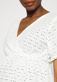 White dress made of textured fabric, featuring a V-neck, short puff sleeves, and open eyelet patterns throughout.
