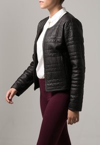 Svart vadderad jacka med en mjuk textur, med rundad halsringning och långa ärmar, i kombination med burgundy leggings och en vit skjorta.