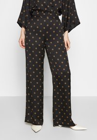 Black wide-leg pants in a silky fabric, featuring small orange circular patterns, with a high waist and subtle sheen.