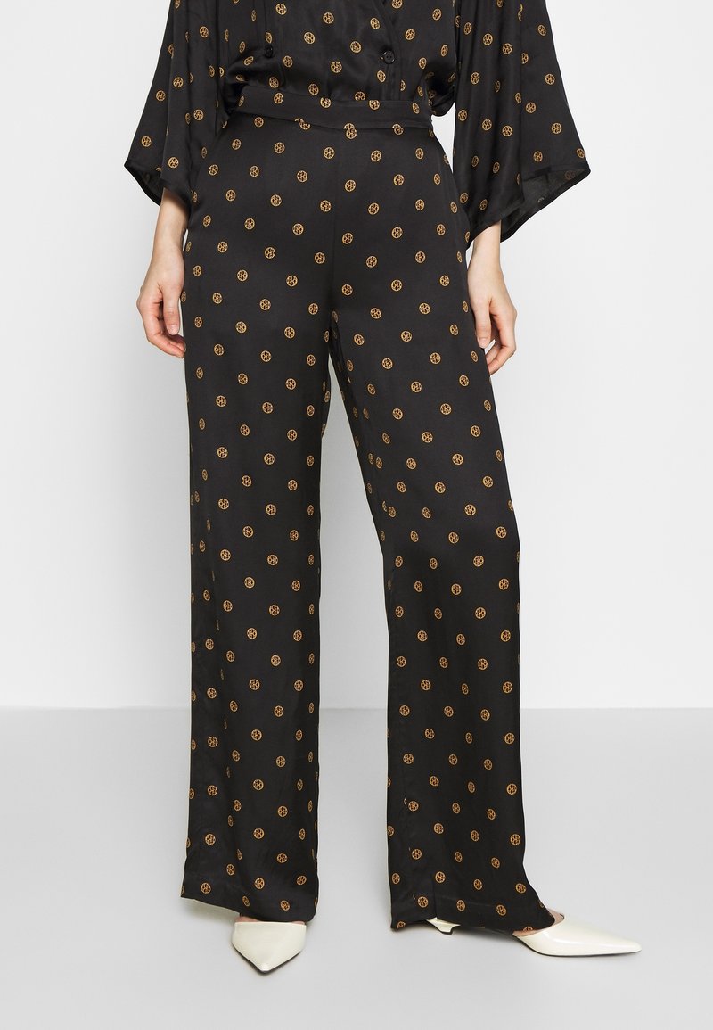 Black wide-leg pants in a silky fabric, featuring small orange circular patterns, with a high waist and subtle sheen.