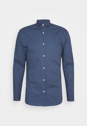 Dlouhý rukáv košile v námořnické modři s malým opakujícím se bílým geometrickým vzorem. Má špičatý límec a bílé knoflíky. Hladká textura.