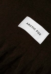Tissu tricoté texturé brun foncé avec une étiquette blanche affichant "ARCTIC FOX" en noir. L'étiquette est cousue dans le matériau.