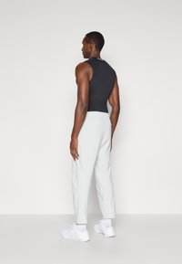 Μαύρο αμάνικο μπλουζάκι και ανοιχτό γκρι παντελόνι με ελαστική μέση, άτομο που στέκεται με την πλάτη στην κάμερα, λευκά αθλητικά παπούτσια, απλός σχεδιασμός.