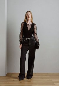 Top lungo a maniche nere in rete con scollatura ondulata abbinato a jeans neri a gamba larga a vita alta e una cintura nera spessa, che mette in risalto il punto vita.