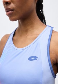 Κοντινό πλάνο ενός ατόμου που φοράει αθλητική φανέλα ανοιχτού γαλάζιου με μπλε λογότυπο στο στήθος και πλεξούδες μακριά τραβηγμένες προς τα πίσω.