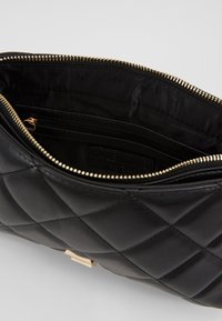 Interno di una borsa in pelle trapuntata nera con zip dorata. Presenta una fodera in tessuto e una piccola tasca con zip per l'organizzazione.