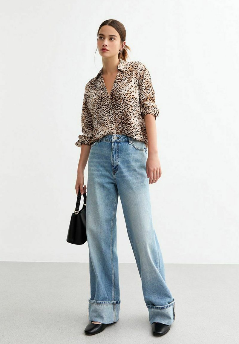 Camicia a bottoni con stampa leopardata e maniche arrotolate, abbinata a jeans a gamba larga blu chiaro, borsa nera e tacchi a punta.